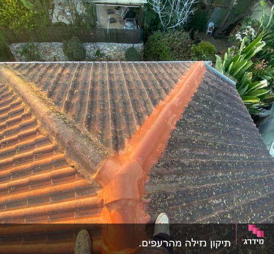 אדם עומד על גג רעפים עם חומר איטום כתום